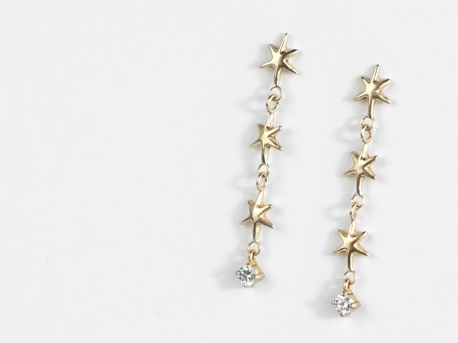 Long gold earrings made of up 3 linked stars and a hanging single diamond