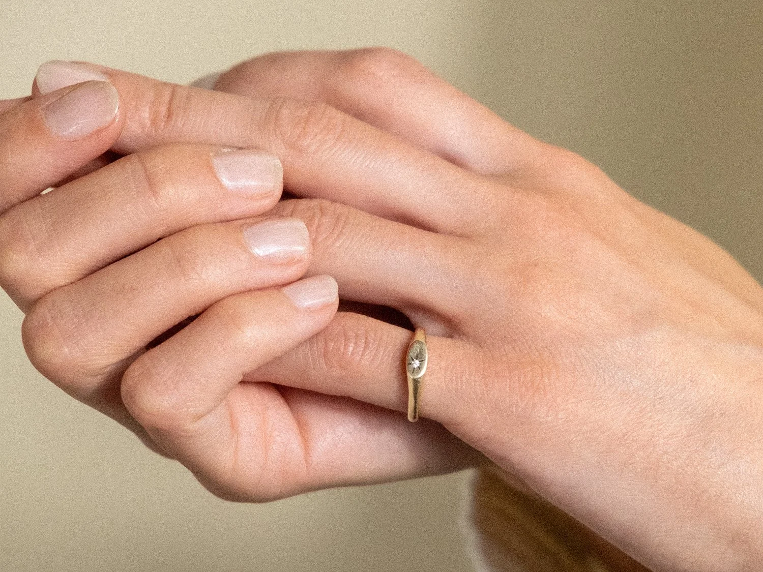 Model's hand wearing a gold pinky signet ring with a single diamond set in a star shape