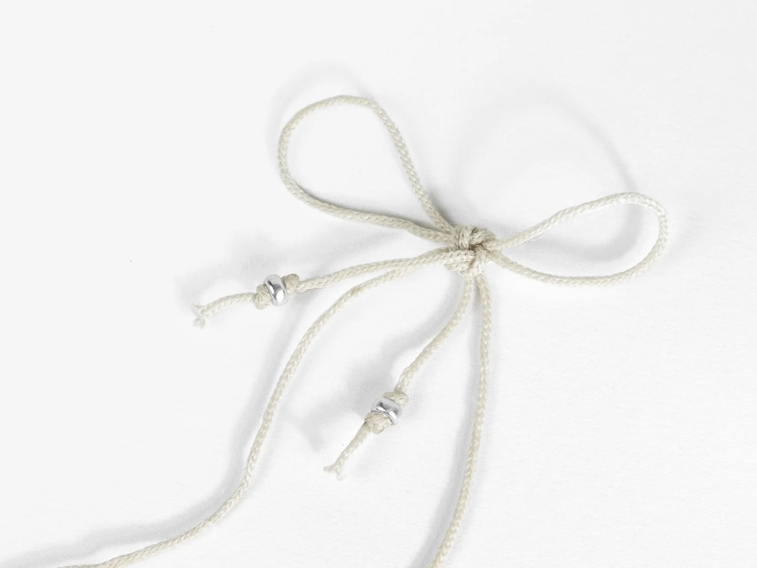 Ivory braided cord tied in a bow with silver beads knotted onto each end
