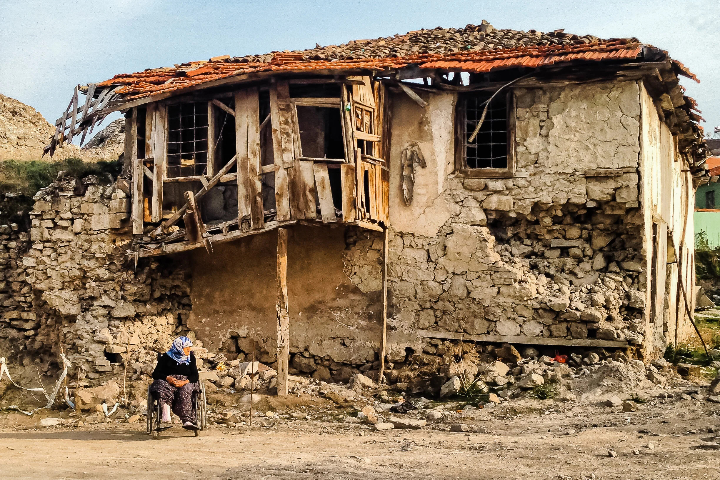 Woman in a wheelchair in front an abandoned, ruin of a house. Burdur, Turkey.