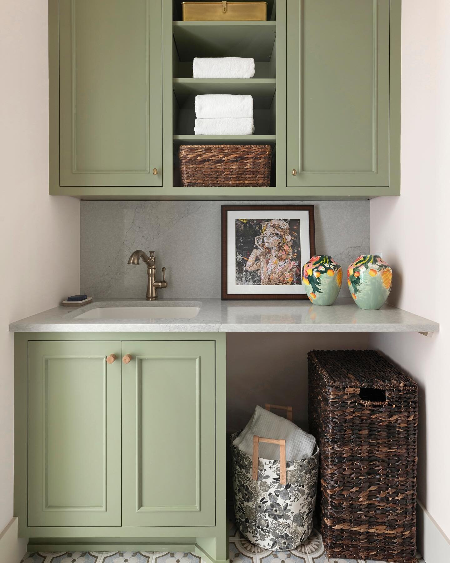 This charming, whimsical laundry nook features a prep-space with soft neutral tones + stunning green cabinetry making this space feel polished and contemporary. Take note of the under-cabinet storage space where you can keep an extra clothes basket +