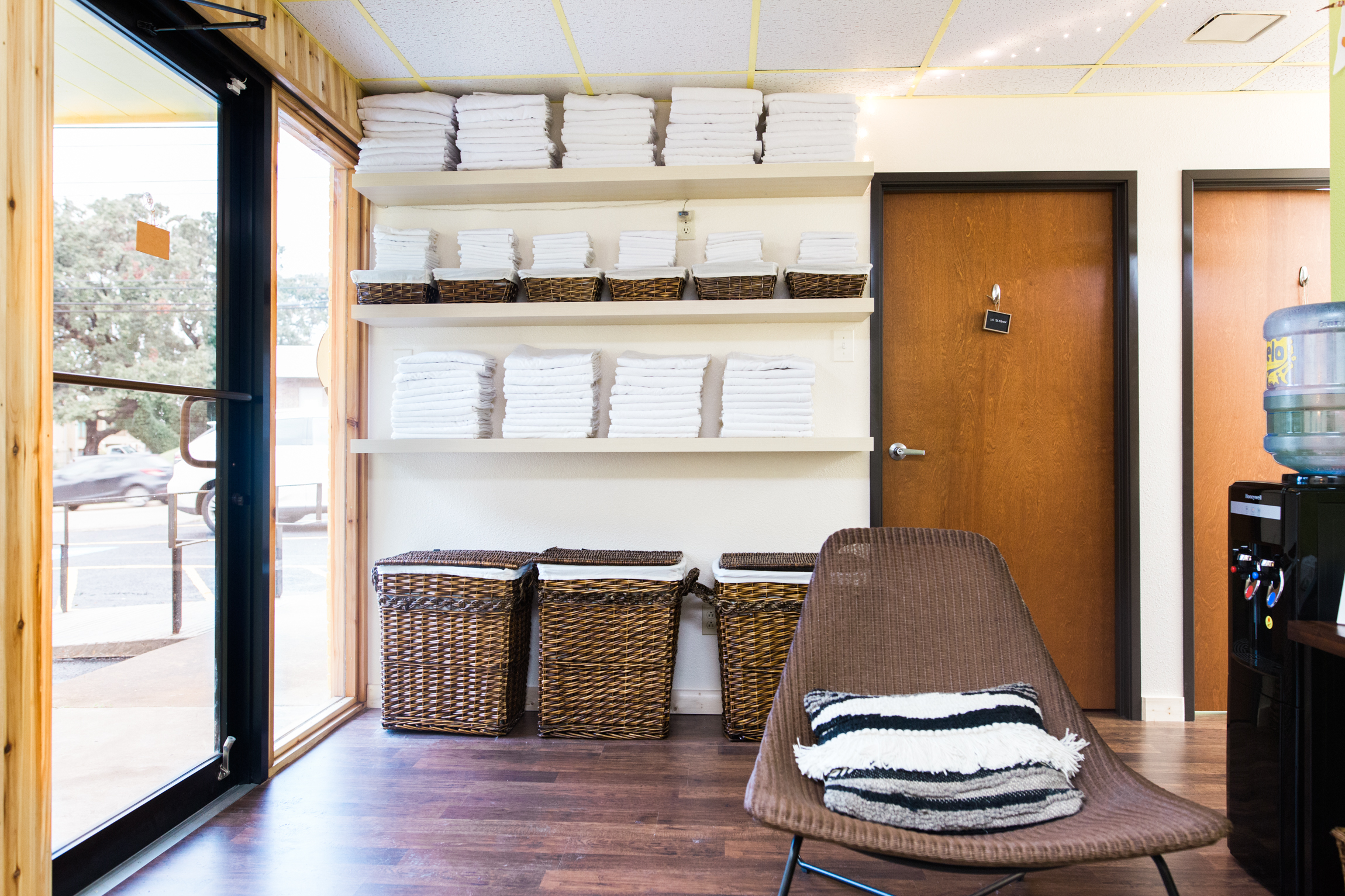  Image featuring the waiting area at Mantis Massage Therapy Studio in Austin, Texas. Captured in this invited image is freshly laundered linens and towels, neatly stacked on a shelf, promising a hygienic and luxurious massage experience. Sunlight str