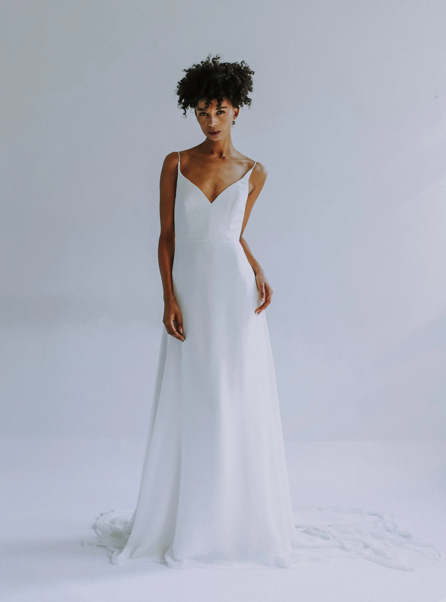 light ivory sweethearted V-neck bodice gown with slim A-line skirt in silk georgette. Fully boned bodice with spa- ghetti straps. Long train. Closes with zipper up the back.