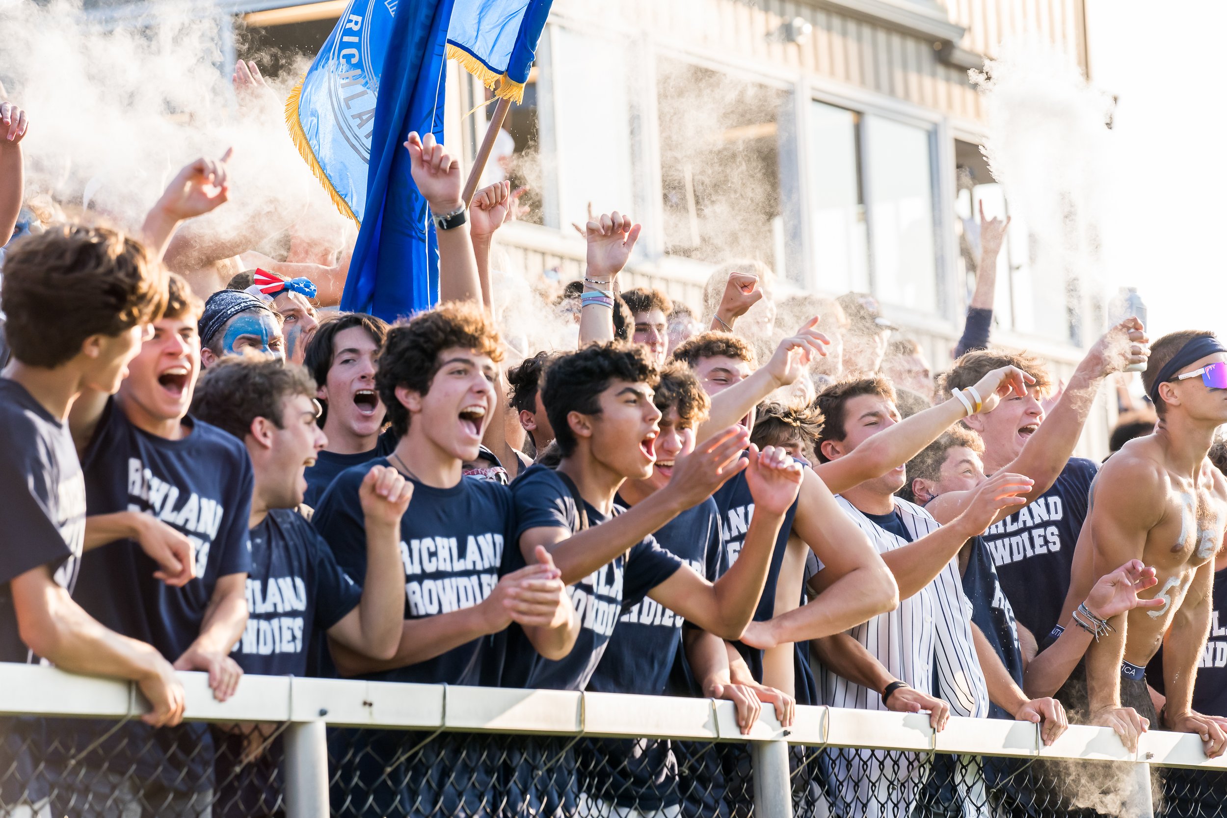 Group of students in bleachers cheering during sports game.