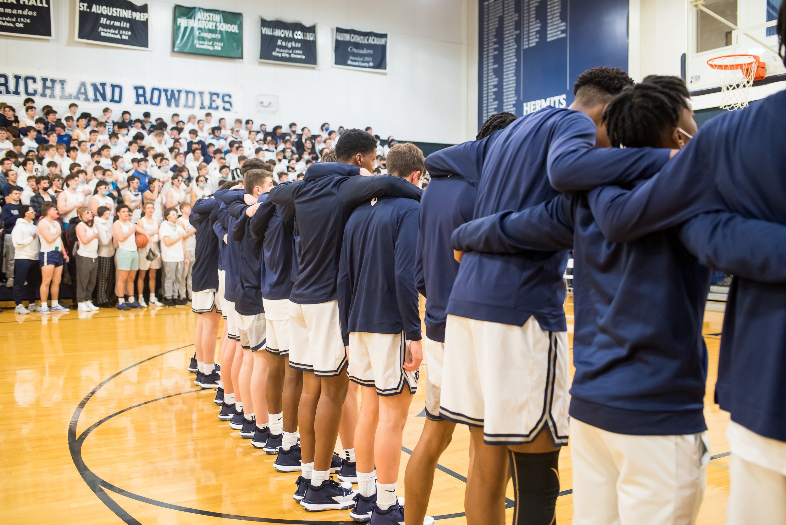 Hermits Basketball team lines up in front of crowd in the school gymnasium prior to a game.