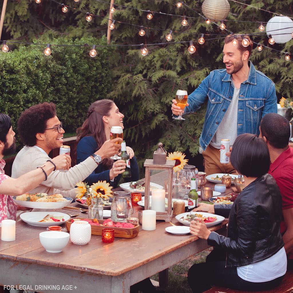 Barbecue Season, Stella Artois. People gathered around an outdoor table holding glasses of beer.
