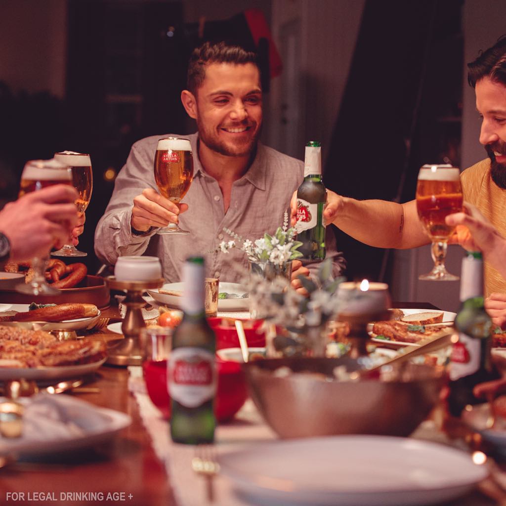 Dinner Party, Stella Artois. People are cheering with glasses of beer.