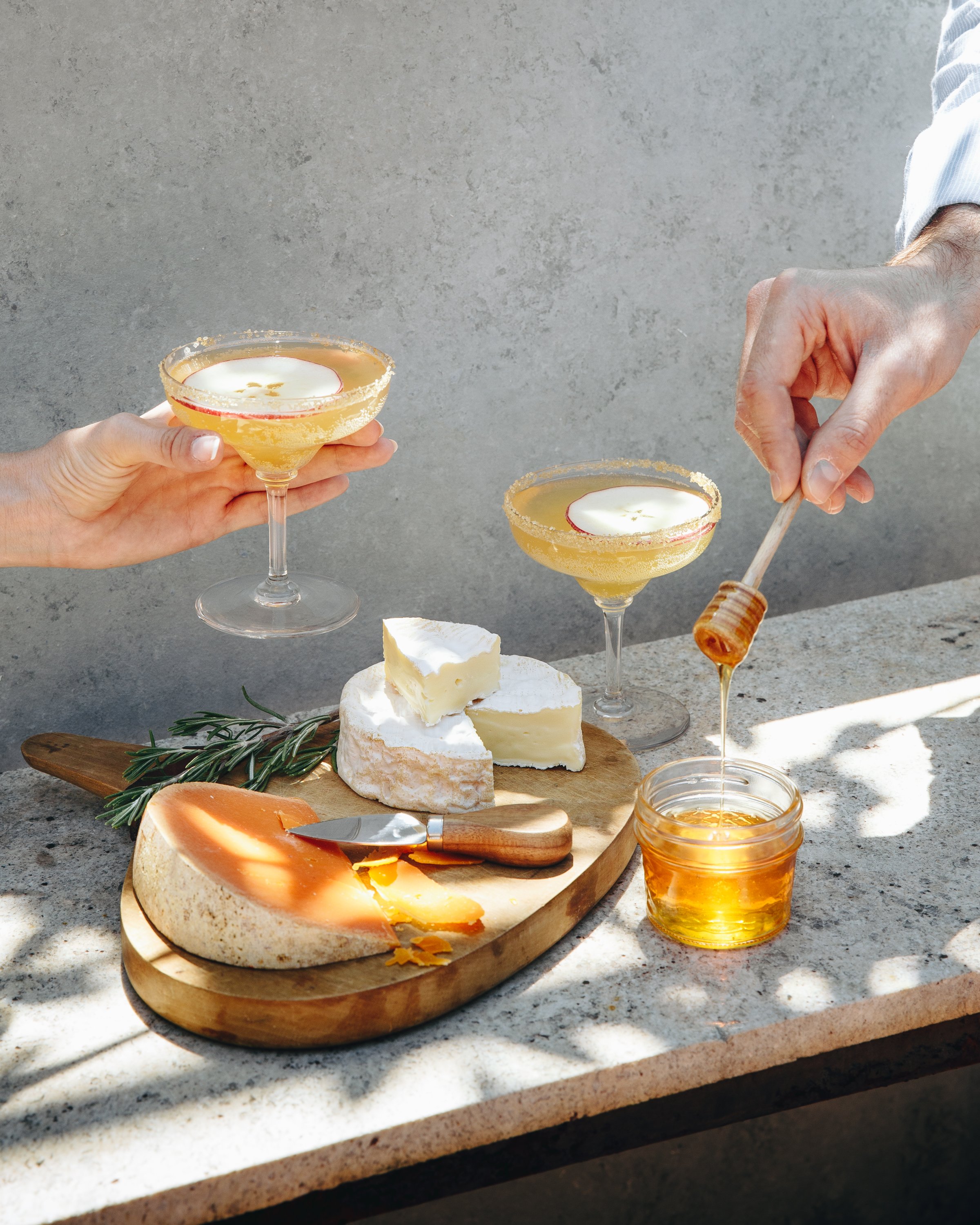 A cheese platter with honey and two cocktails
