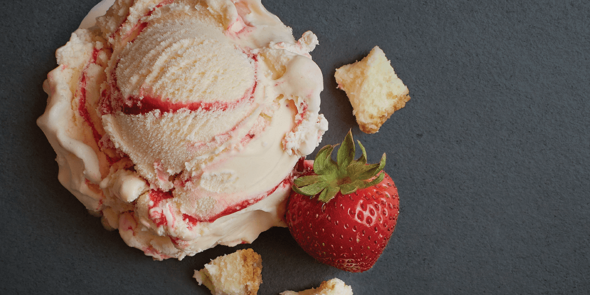 A scoop of strawberry shortcake ice cream with a berry and pieces of cake around it.