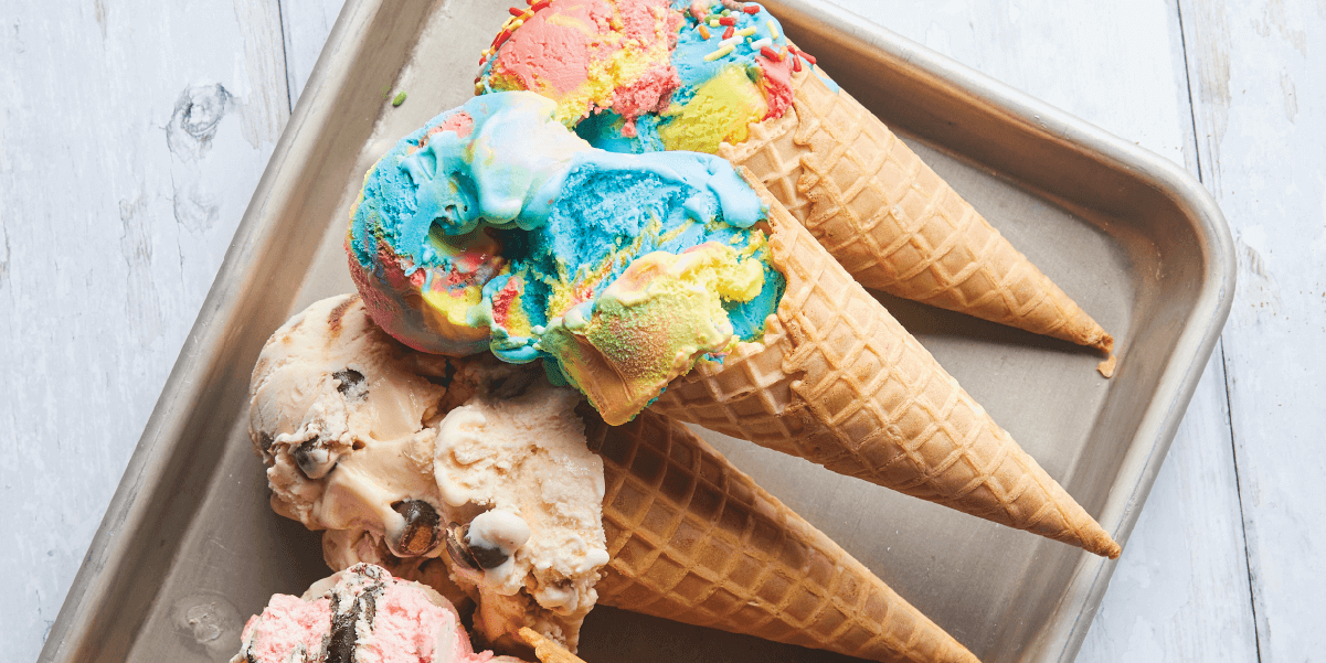 Cones of ice cream on a sheet tray. Many flavors.