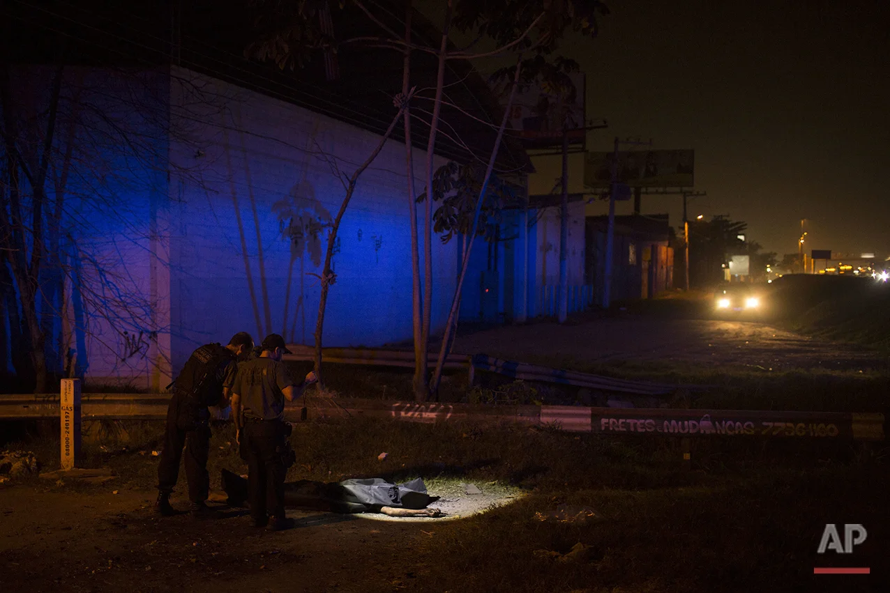 In this July 15, 2016 photo, police officers use a flashlight to inspect the crime scene where the body of an alleged thief was found on a roadside in Nova Iguacu, greater Rio de Janeiro, Brazil. Gruesome scenes of death and impunity play out daily in Rio's hundreds of shantytowns, known as favelas. (AP Photo/Felipe Dana)