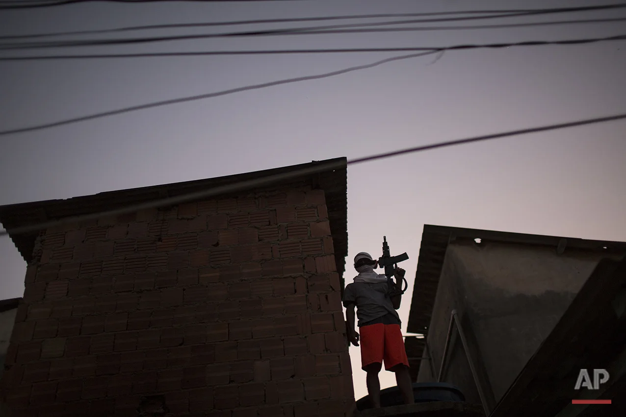 In this July 11, 2016 photo, a young drug trafficker poses for a photo holding his weapon at a slum in Rio de Janeiro, Brazil. Teenagers openly tote guns while they work as guards, lookouts and distributors for drug lords operating just a few miles (kilometers) from where hundreds of thousands and tourists and athletes will be for the Aug. 5-21 Olympic Games. (AP Photo/Felipe Dana)
