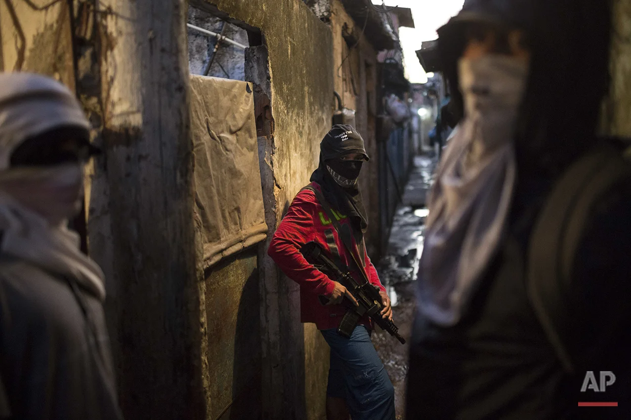 In this July 11, 2016 photo, masked teenage boys pose for photos holding their guns at a slum in Rio de Janeiro, Brazil. The teens are security guards, lookouts and distributors for drug lords operating just a few miles (kilometers) from where hundreds of thousands and tourists and athletes will be for the Aug. 5-21 Olympic Games. (AP Photo/Felipe Dana)
