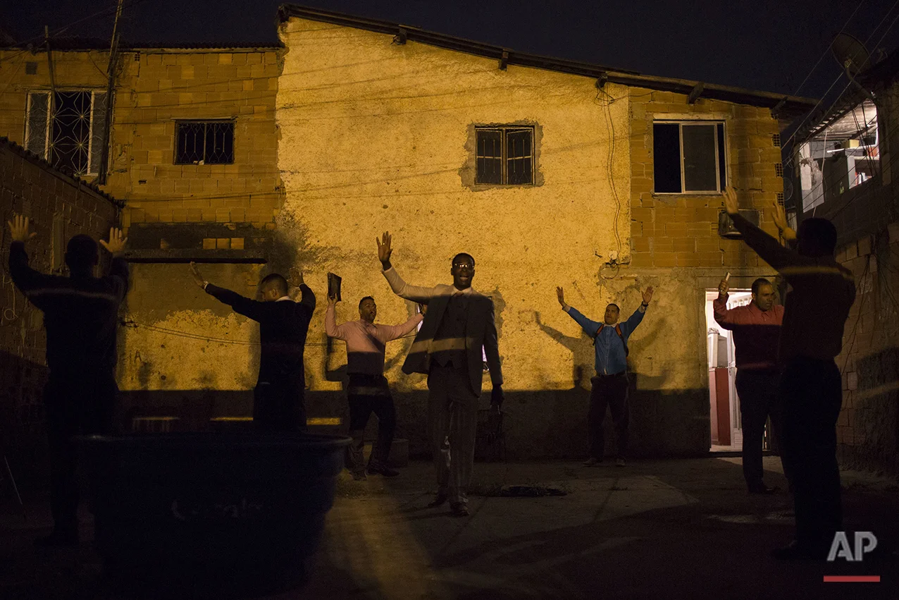 In this July 16, 2016 photo, Pastor Nilton, back right in blue, rejoices with members of his church after learning that residents will allow him to hold a prayer service in their courtyard, in a gang-ruled slum in Rio de Janeiro, Brazil. Pastor Nilton, a former drug trafficker, spends his energy looking to convert the teenage boys who serve as security guards, lookouts and distributors for the drug lords operating in the slums. (AP Photo/Felipe Dana)