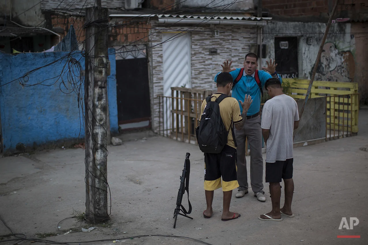 In this July 16, 2016 photo, pastor Nilton blesses two young drug traffickers at a slum in Rio de Janeiro, Brazil. Many of the young drug traffickers have an immense respect for the pastor, a former drug trafficker. It's not uncommon to see young men set their weapons down, but only long enough to receive his blessing. (AP Photo/Felipe Dana)