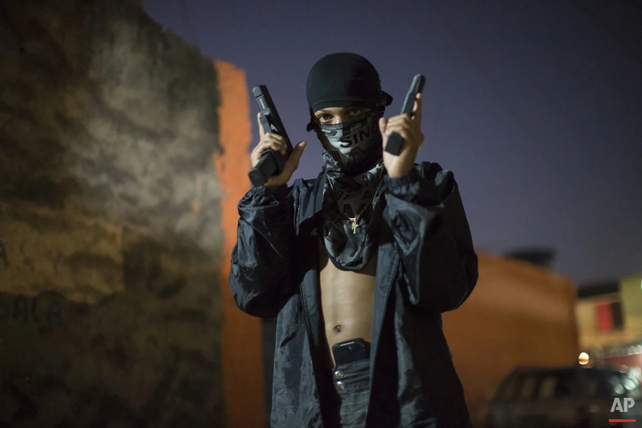 In this July 11, 2016 photo, a young, masked drug trafficker poses for photos holding his guns at a slum in Rio de Janeiro, Brazil. (AP Photo/Felipe Dana)