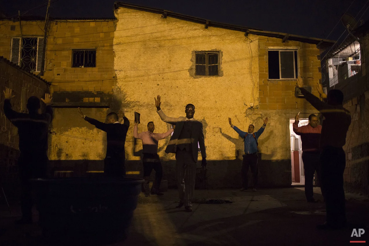 In this July 16, 2016 photo, Pastor Nilton, back right in blue, rejoices with members of his church after learning that residents will allow him to hold a prayer service in their courtyard, in a gang-ruled slum in Rio de Janeiro, Brazil. Pastor Nilton, a former drug trafficker, spends his energy looking to convert the teenage boys who serve as security guards, lookouts and distributors for the drug lords operating in the slums. (AP Photo/Felipe Dana)