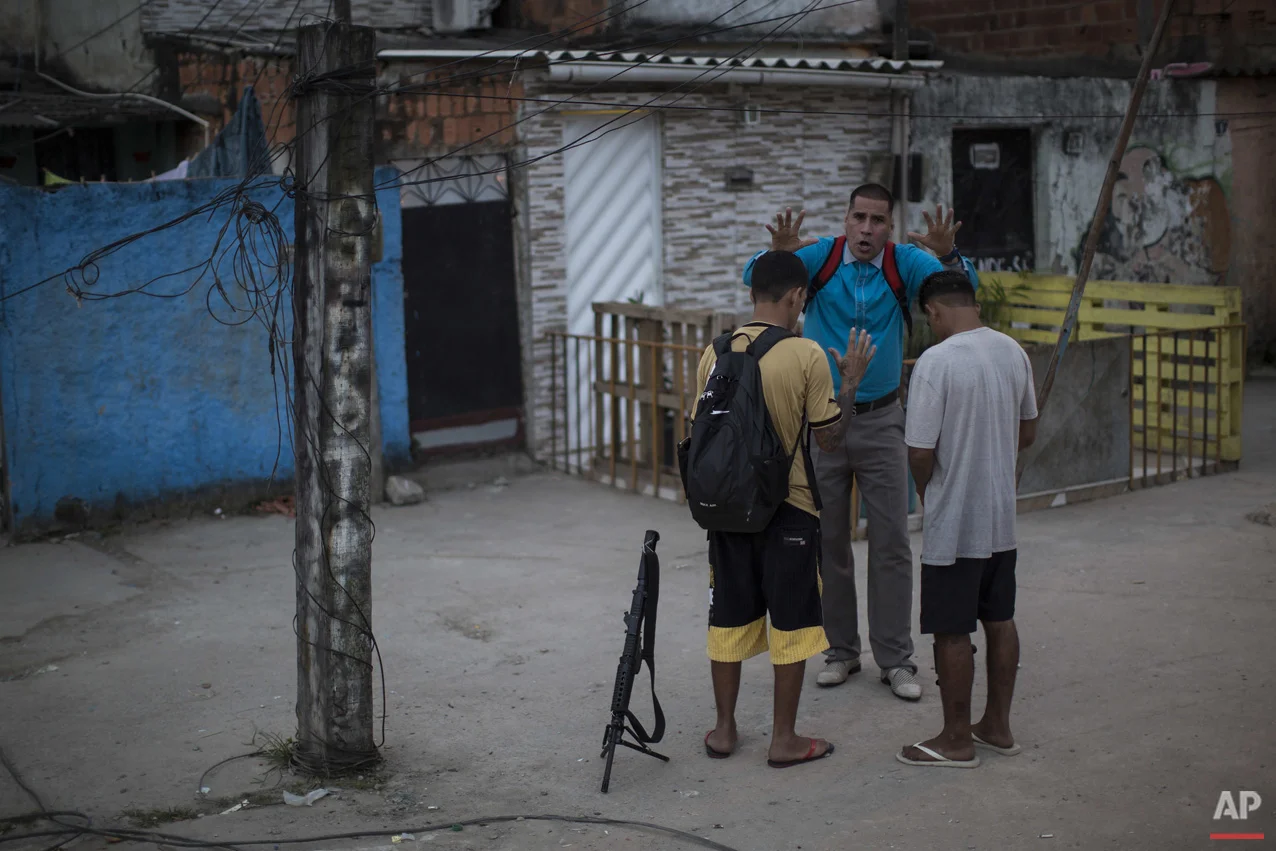 In this July 16, 2016 photo, pastor Nilton blesses two young drug traffickers at a slum in Rio de Janeiro, Brazil. Many of the young drug traffickers have an immense respect for the pastor, a former drug trafficker. It's not uncommon to see young men set their weapons down, but only long enough to receive his blessing.(AP Photo/Felipe Dana)