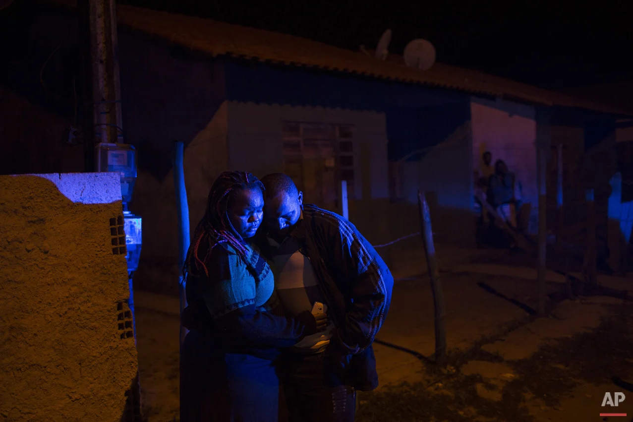 In this July 13, 2016 photo, an eyewitness stands with a woman outside a bar where a pre-candidate for local council was shot dead in Mage, in greater Rio de Janeiro, Brazil. According to local news reports the 49-year-old woman was shot by four gunmen while in a bar with a friend and her partner. The woman is the 11th politician murdered in the greater Rio area since November, and police have not been able to determine the motives for the killings. (AP Photo/Felipe Dana)