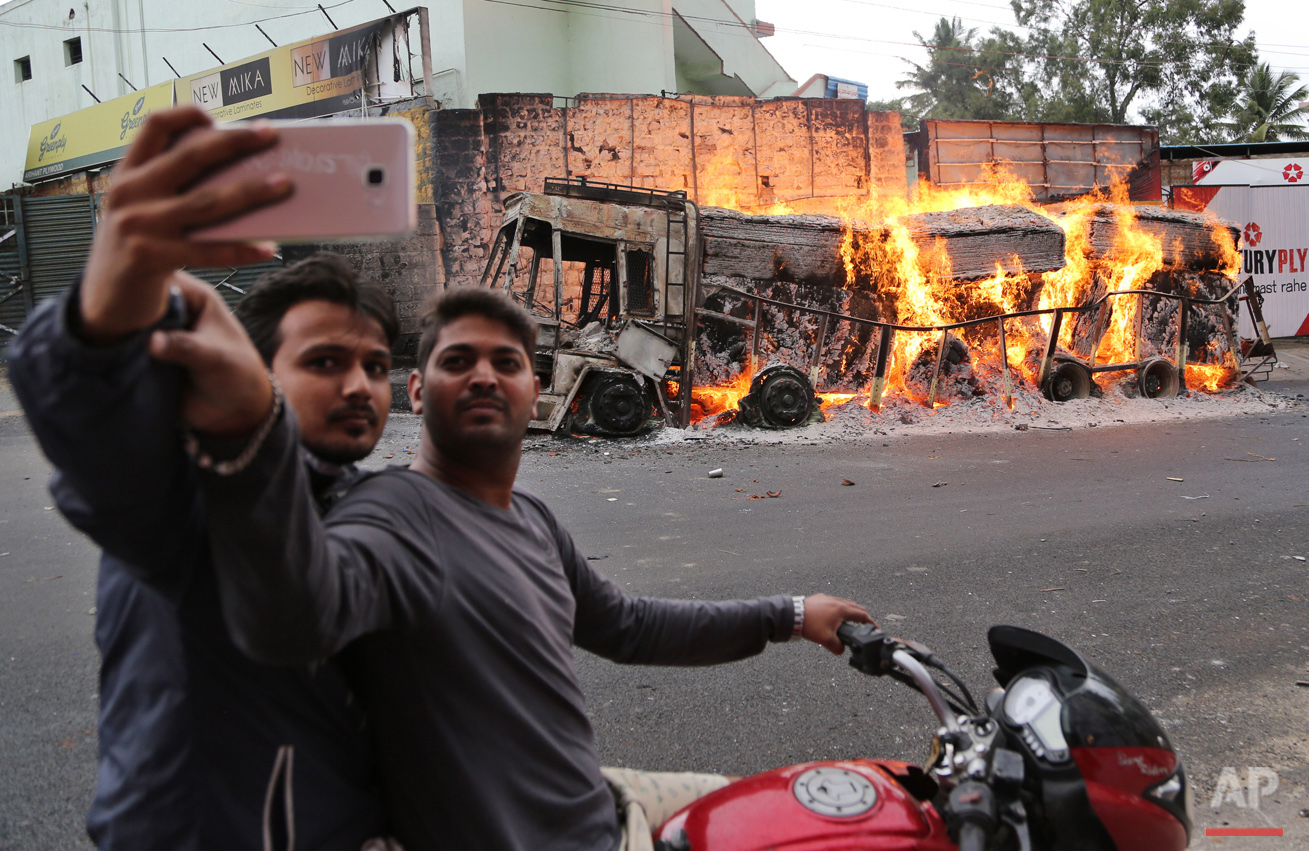  Two men on a motorcycle stop to take a selfie with a burning truck from neighboring Tamil Nadu state, after it was set ablaze by angry mobs in Bangalore, Karnataka state, India, Monday, Sept. 12, 2016. India's top court on Monday ordered the souther