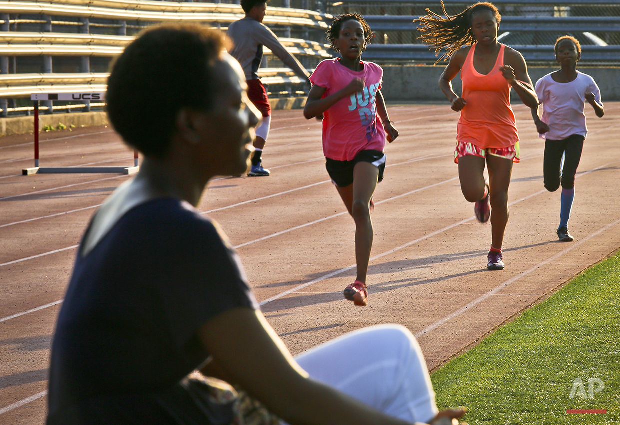  In this Wednesday, July 20, 2016 photo, Tonia Handy, far left, sits near the track during an interview as her daughters Rainn Sheppard, 10, second from left, and Brooke Sheppard, 8, far right, run during track practice at Boys and Girls High School 