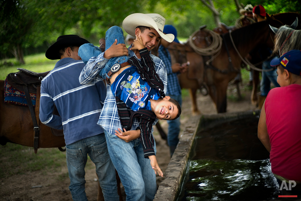  In this July 29, 2016 photo, a cowboy playfully threatens to dunk a younger boy into a water troff, during an improvised rodeo event at a farm in Sancti Spiritus, central Cuba. In the flat grasslands in the central province of Sancti Spiritus, a gro