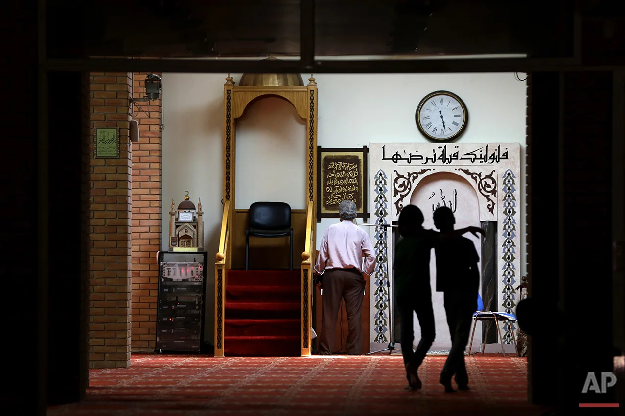  A man prays as two children walk at the Greek-Arab Cultural Center, a muslim prayer site in Athens, Thursday, Aug. 4, 2016. Lawmakers in Greece have approved construction of a state-funded mosque near central Athens, a proposal that triggered dissen