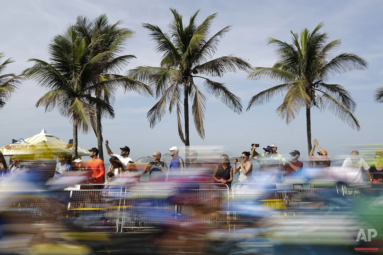 In this photo taken with a slow shutter speed, people watch as cyclists ride past them on Ipanema beach during the men's cycling road race final at the 2016 Summer Olympics in Rio de Janeiro, Brazil, Saturday, Aug. 6, 2016. (AP Photo/Felipe Dana)