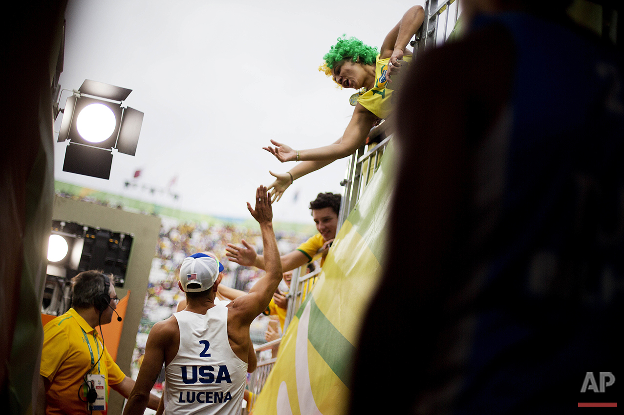 Nicholas Lucena, of the United States, high-fives fans as he takes the court with teammate Philip Dalhausser to play Tunisia in a men's beach volleyball match at the 2016 Summer Olympics in Rio de Janeiro, Brazil, Sunday, Aug. 7, 2016. (AP Photo/David Goldman)