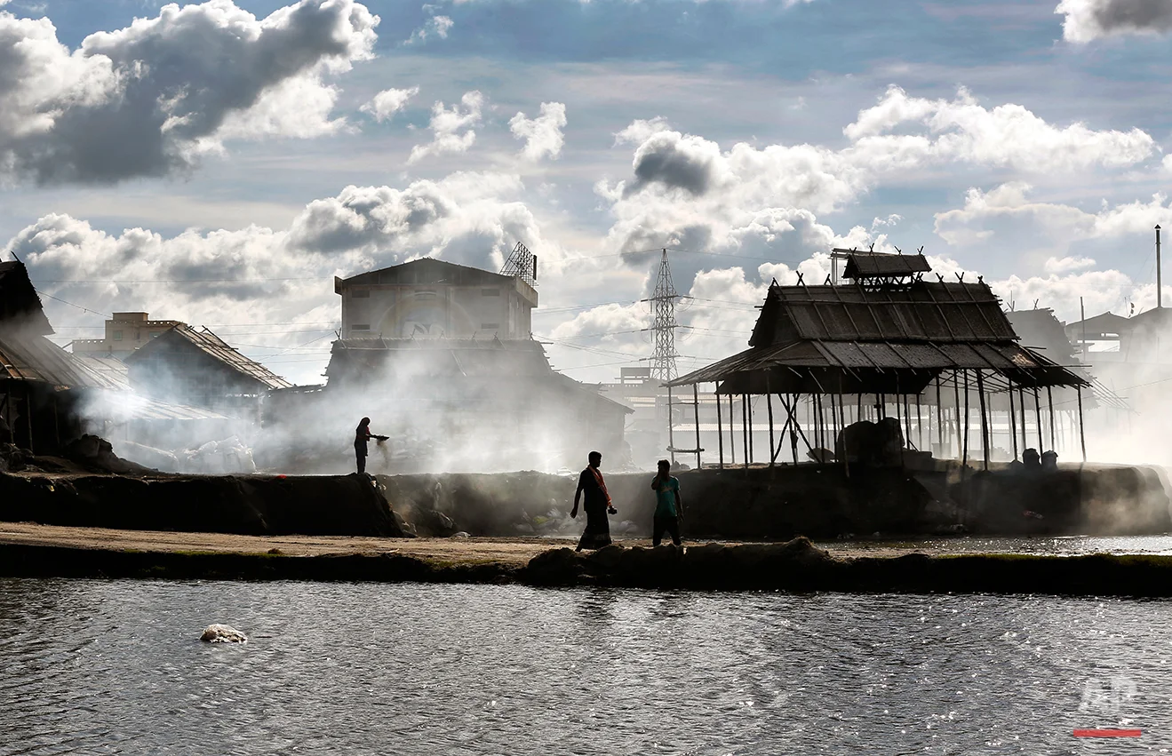 In this Aug. 3, 2016 photo, a Bangladeshi woman stands in rising smoke as she sorts aluminum pieces from industrial waste on the outskirts of Dhaka, Bangladesh. A large swath of land not far from the Buriganga River is dotted with makeshift tents that are home to men and women who travel far from home to work 12 hours a day recycling cans, industrial ash and medicine blister packets into raw aluminum. The work is difficult and dangerous. The workers have no safety equipment or masks to protect themselves from the fumes and aluminum dust. (AP Photo/ A.M. Ahad)