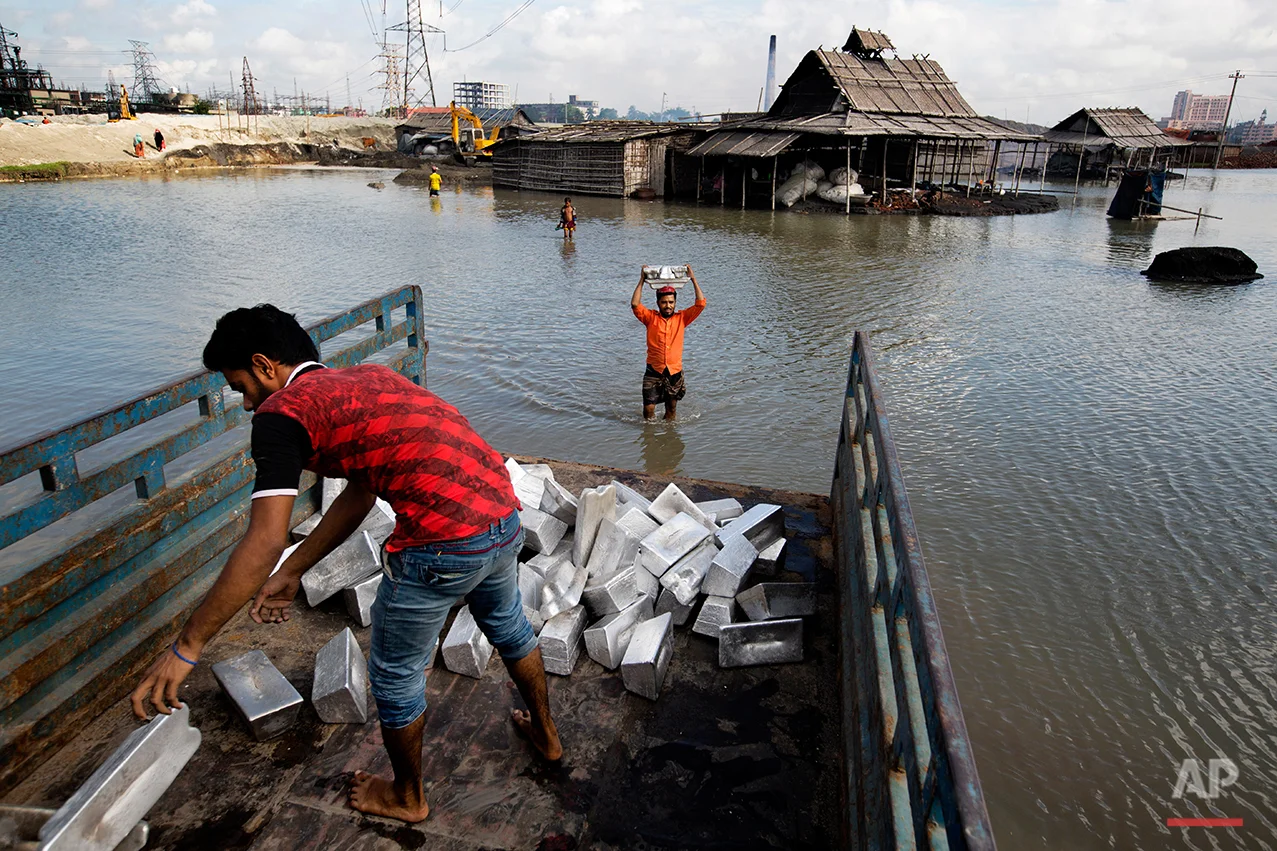 In this Aug. 3, 2016 photo, recycled blocks of aluminum are loaded for transportation to a market from an aluminum recycling factory on the outskirts of Dhaka, Bangladesh. A large swath of land not far from the Buriganga River is dotted with makeshift tents that are home to men and women who travel far from home to work 12 hours a day recycling cans, industrial ash and medicine blister packets into raw aluminum. The work is difficult and dangerous. The workers have no safety equipment or masks to protect themselves from the fumes and aluminum dust. (AP Photo/A.M. Ahad)