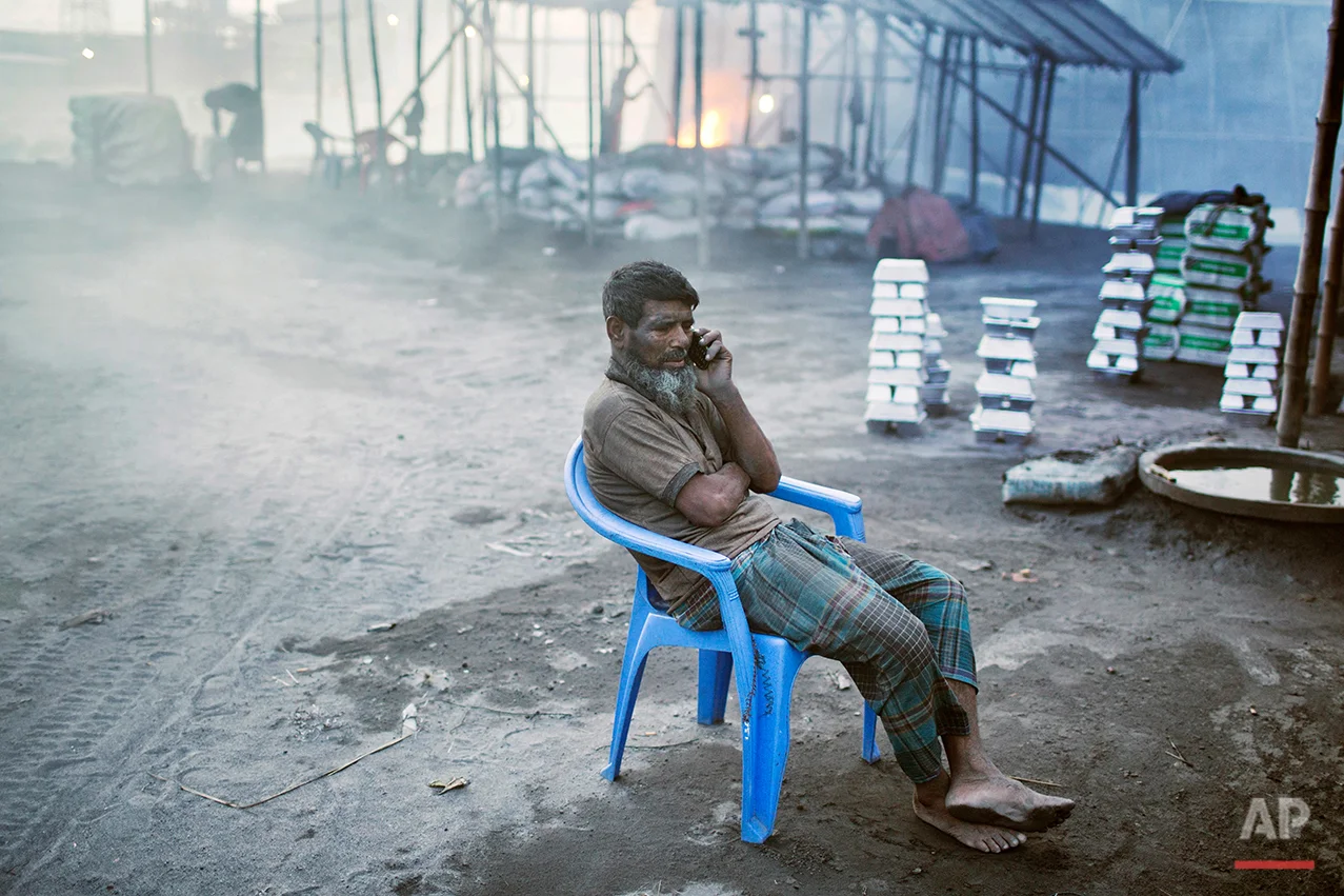 In this Aug. 6, 2016 photo, Mohammad Motaleb, an aluminum recycling factory worker, talks to his daughter during a break on the outskirts of Dhaka, Bangladesh. A large swath of land not far from the Buriganga River is dotted with makeshift tents that are home to men and women who travel far from home to work 12 hours a day recycling cans, industrial ash and medicine blister packets into raw aluminum. The work is difficult and dangerous. The workers have no safety equipment or masks to protect themselves from the fumes and aluminum dust. (AP Photo/ A.M. Ahad)