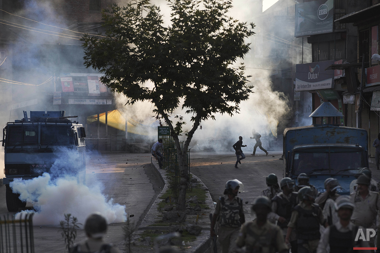 Kashmiri Muslim protesters run for cover from plumes of tear gas as Indian paramilitary soldiers walk back towards their base camp after a day-long curfew in Srinagar, Indian controlled Kashmir, Monday, Aug. 8, 2016. Kashmir has been under a security lockdown and curfew since the killing of a popular rebel commander on July 8 sparked some of the largest protests against Indian rule in recent years. (AP Photo/Dar Yasin)