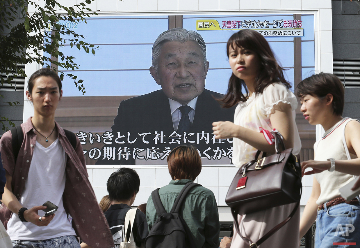 Pedestrians walk past a screen as Emperor Akihito delivers a speech in Tokyo, Monday, Aug. 8, 2016. Akihito, in a rare address to the public, signaled his apparent wish to abdicate by expressing concern about his ability to fully carry out his duties. (AP Photo/Koji Sasahara)