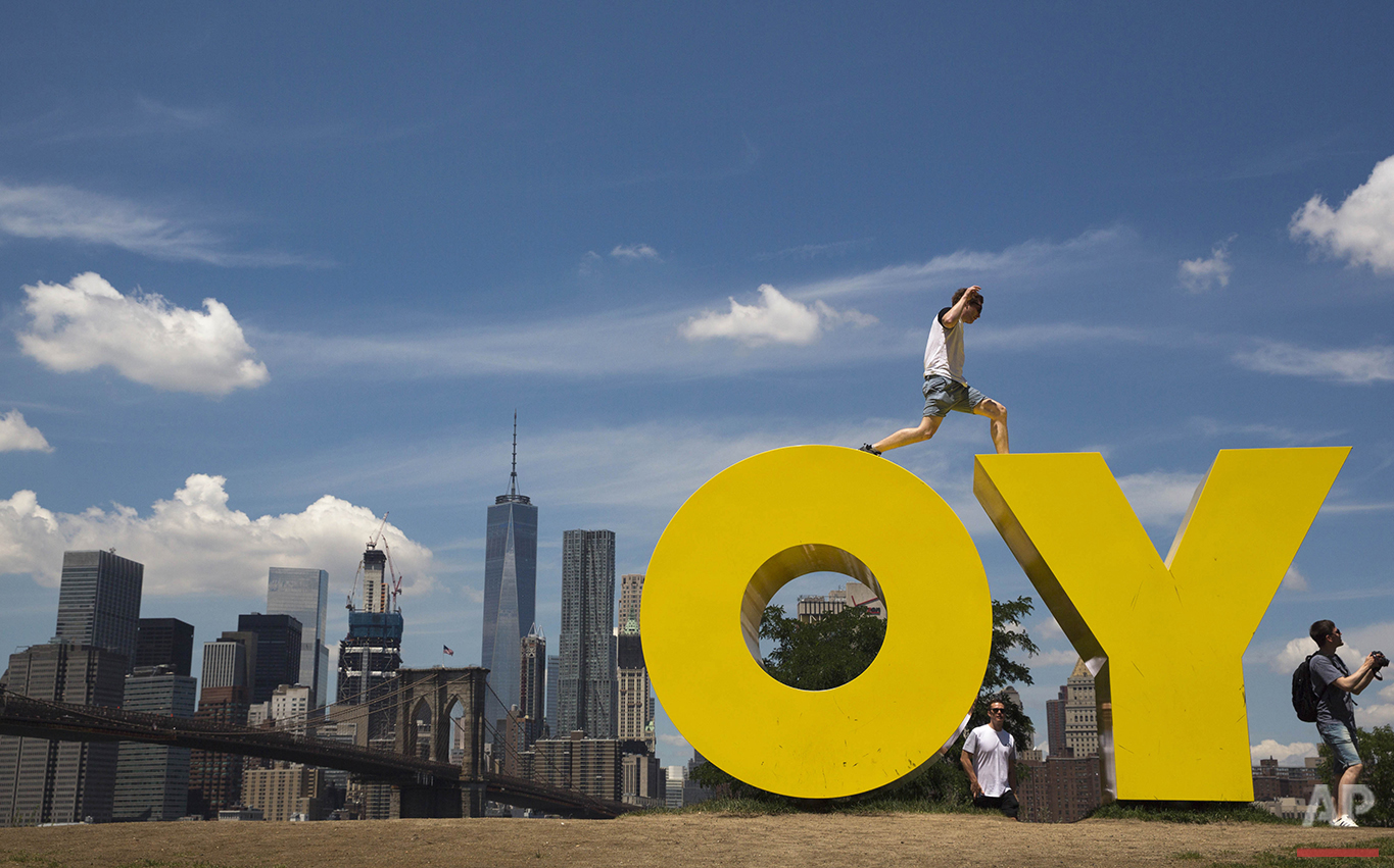 A visitor to the Brooklyn Bridge park jumps between the letters in Deborah Kass' sculpture OY/YO in New York on Thursday, June 30, 2016. (AP Photo/Mary Altaffer)