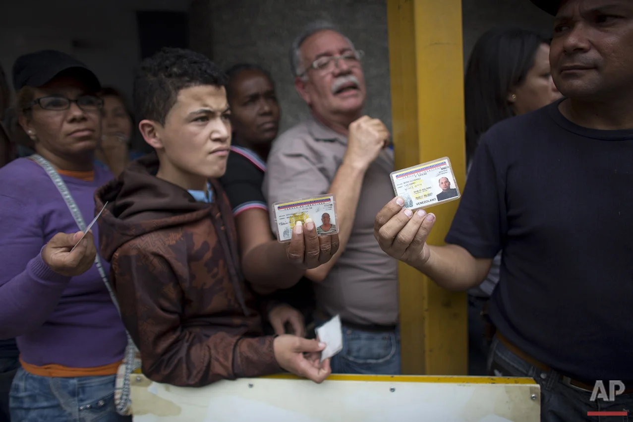  In this Tuesday, May 3, 2016 photo, people show their national ID cards as they wait in line outside a supermarket to buy food in Caracas, Venezuela. All Venezuelans, including children, are assigned two shopping days a week based on their state ID 