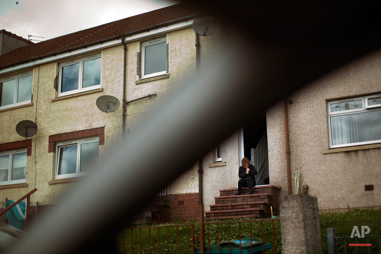  In this Saturday, July 2, 2016 photo, a woman lights a cigarette as she sits on the steps of her house in Motherwell, southeast of Glasgow, Scotland. Motherwell, belongs to a council area where 62 percent of voters backed remaining in the EU. Places
