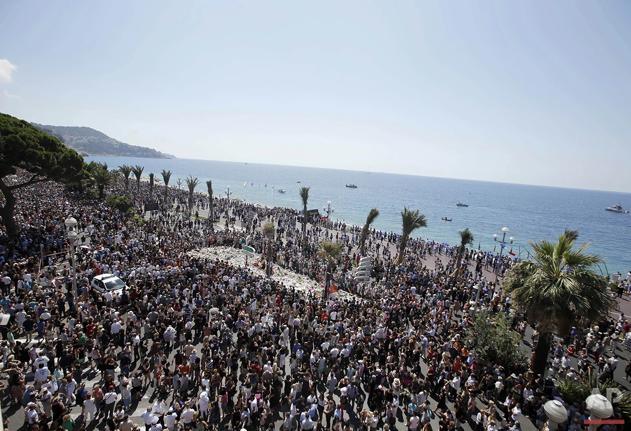 People gather at a makeshift memorial to observe a minute of silence to honor the victims of an attack near the area where a truck mowed through revelers on the Promenade des Anglais in Nice, southern France, Monday, July 18, 2016. Eighty four were killed in the attack during Bastille Day celebrations. (AP Photo/Luca Bruno)