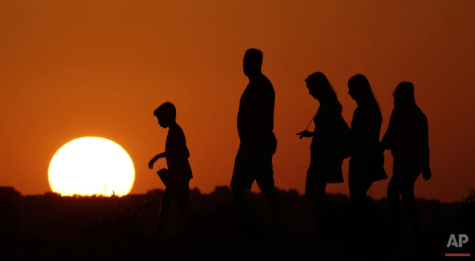 The sun sets behind visitors to Liberty Memorial in Kansas City, Mo., as the temperature hovers around 100 degrees on Thursday, July 21, 2016. The National Weather Service outlook for the next three months shows above normal temperatures across the country. (AP Photo/Charlie Riedel)