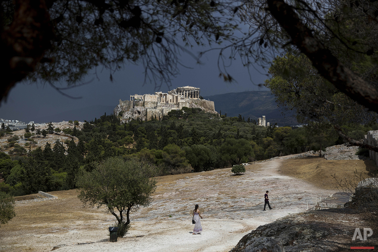  People walk on Pnyx hill in front of the ancient Acropolis hill and the ruins of the fifth century B.C. Parthenon temple in Athens on Tuesday, June 7, 2016. Beginning as early as 507 BC, the Athenians gathered on the Pnyx to host their popular assem