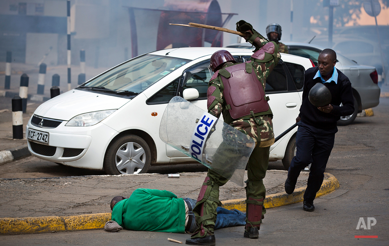  In this photo taken Monday, May 16, 2016, a Kenyan riot policeman beats a protester with a stick, breaking the stick, before kicking him as he lies in the street after falling down while trying to flee from them, during a protest in downtown Nairobi