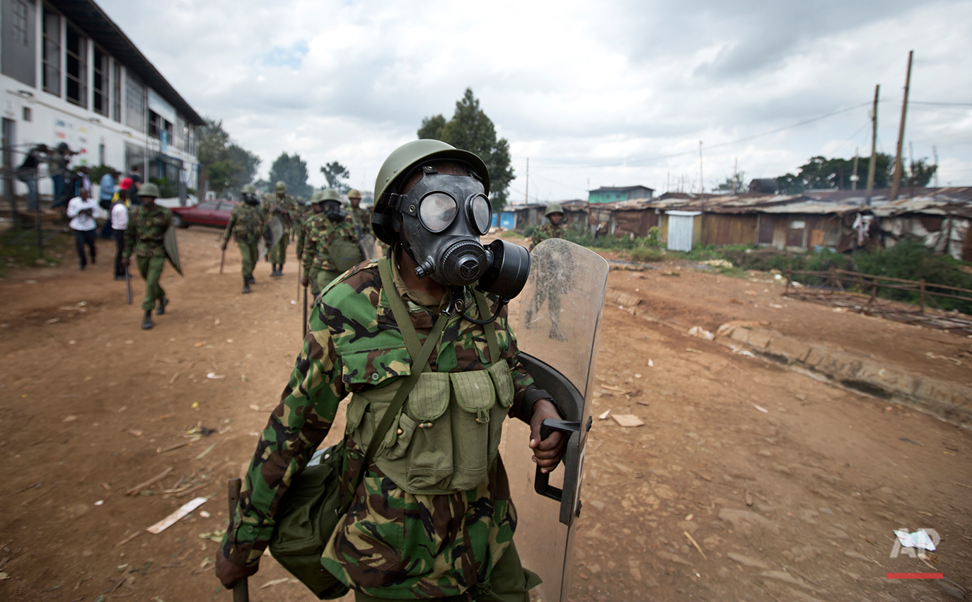  A Kenyan policeman wearing a gas mask chases protesters throwing rocks, in the Kibera slum of Nairobi, Kenya, Monday, May 23, 2016. Kenya's police shot, beat and tear gassed opposition demonstrators across the country who tried to gather to call for