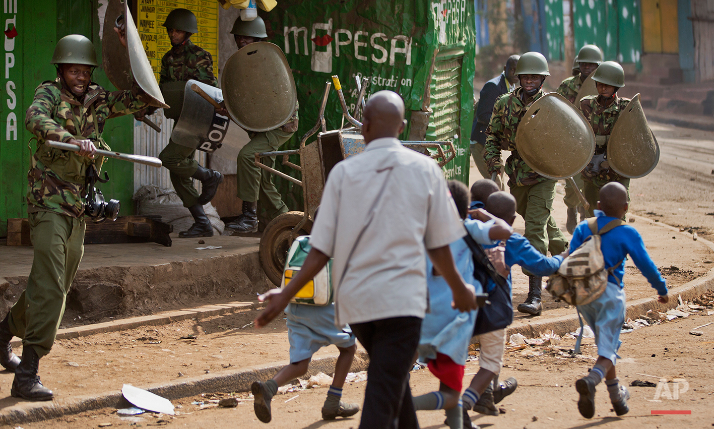 A policeman, left, yells at a man trying to lead schoolchildren to safety, because he was unknowingly about to walk into a hail of rocks thrown by protesters around the corner, as police firing tear gas engage protesters throwing rocks in the Kibera