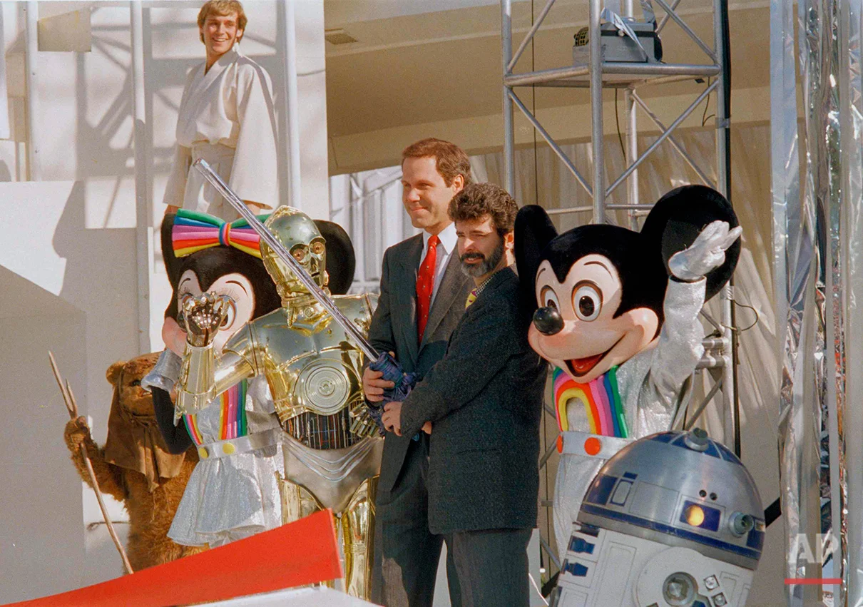 Michael Eisner, center, Disney chairman, and "Star Wars" creator George Lucas (with beard) prepare to use a light saber to cut the ribbon to open the new "Star Tours" attraction at Disneyland in Anaheim, Calif., Jan. 9, 1987. The ride careens people on a spaceship through a star-dodging trip into cinematic outer spac. Characters, from left, are Minnie Mouse, C-3PO, Mickey Mouse and R2-D2. (AP Photo/Bob Galbraith)