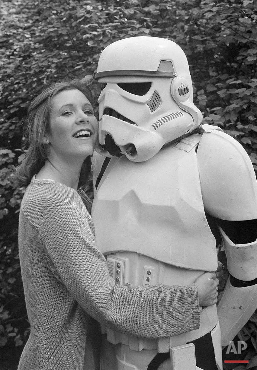 American actress Carrie Fisher, star of the movie "The Empire Strikes Back," sequel to the record-breaking "Star Wars" epic, cuddles up to a Stormtrooper in a London park, May 23, 1980. They were in London to promote the movie. (AP Photo/Dave Caulkin)