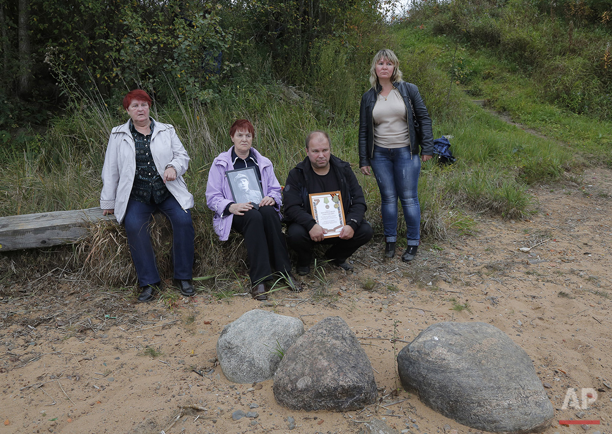  In this photo taken on Friday, Sept. 18, 2015, Tamara Zhukova, left,  and Zoya Izotova, second left, sit at the place where remains of their relatives, Soviet soldiers, were uncovered, at Nevsky Pyatachok near Kirovsk, Russia. Nevsky Pyatachok. The 