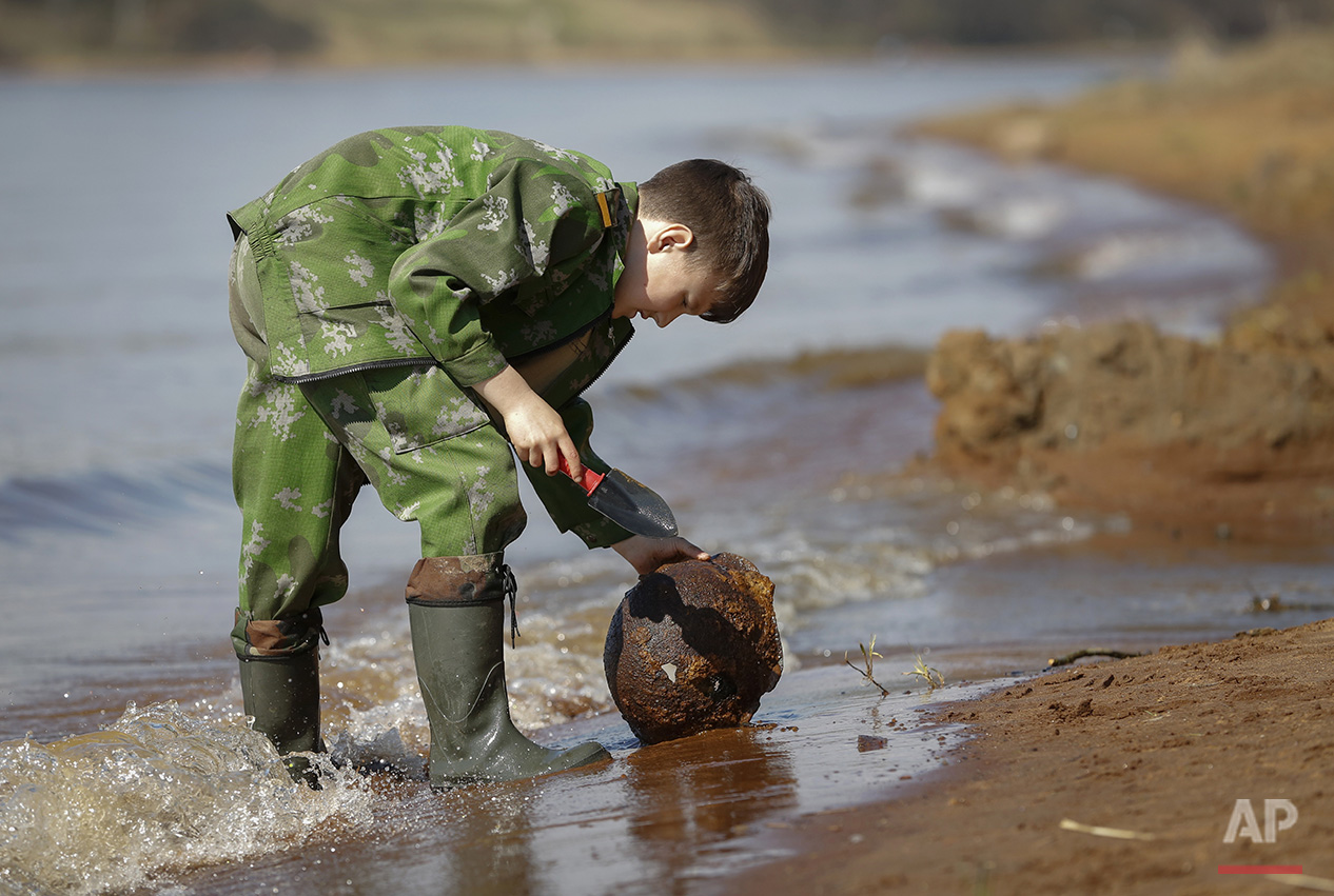  In this photo taken on Monday, May  2, 2016, Gosha, 10-year-old son of a member of a volunteer group searching for the remains of Soviet soldiers killed during WWII, cleans an uncovered WWII Soviet helmet at Nevsky Pyatachok near Kirovsk,  Russia. N