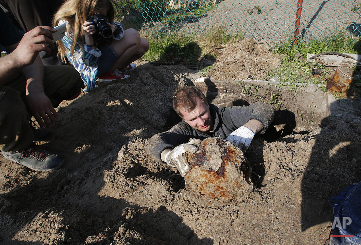  In this photo taken on Tuesday, May  3, 2016,  a member of a volunteer group searching for the remains of Soviet soldiers killed during WWII,  uncovers a helmet of a  Soviet soldier at the yard of a private house at Nevsky Pyatachok near Kirovsk, Ru