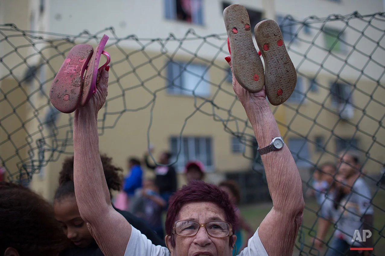  A cheering woman holds up  a pair of sandals as Brazilian judo gold medalist Rafaela Silva is given a hero's welcome into the Cidade de Deus "City of God" slum in Rio de Janeiro, Brazil, Monday, Aug. 22, 2016. Silva who grew up in the violent, pover