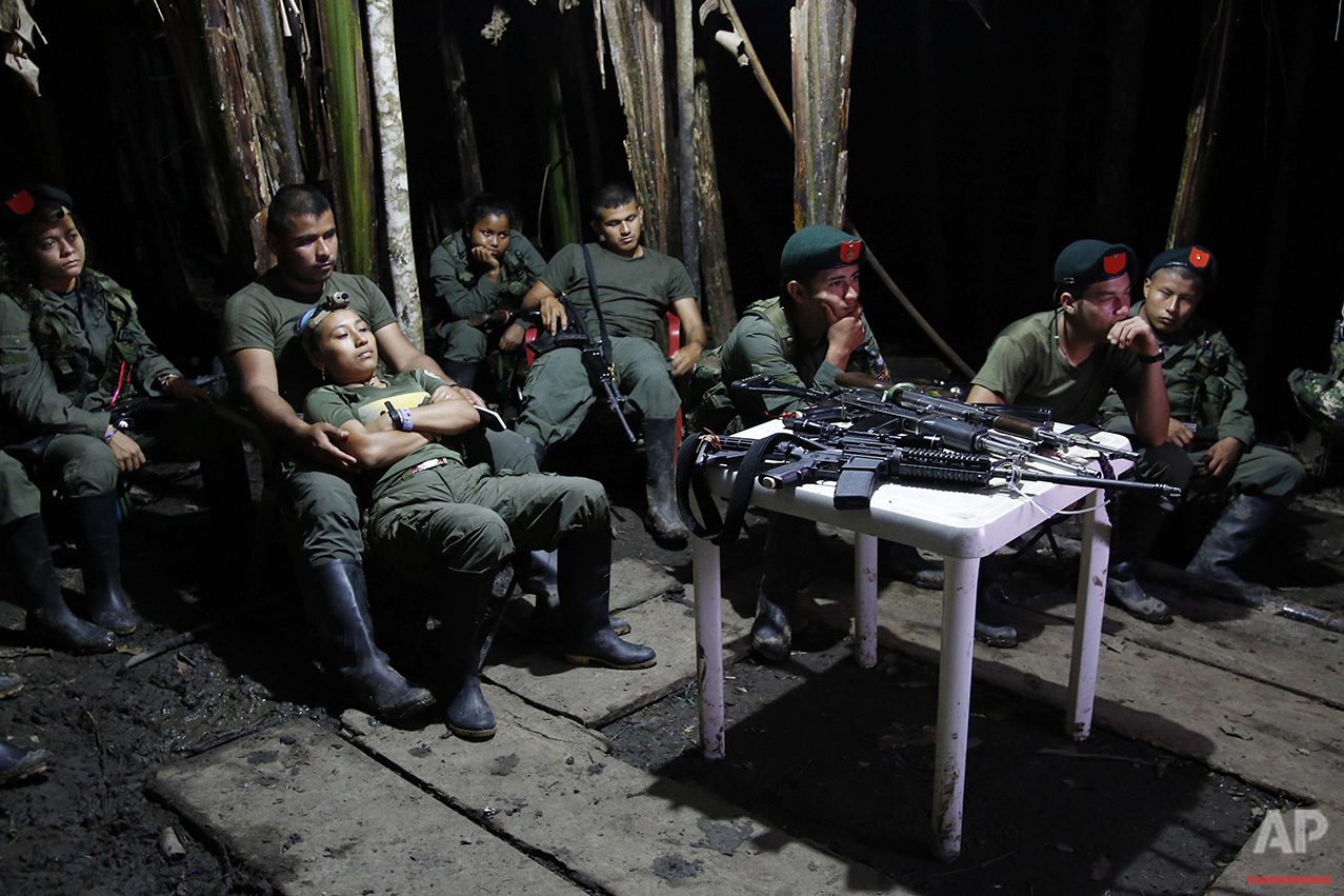  In this Aug. 11, 2016 photo, rebels of the 48th Front of the Revolutionary Armed Forces of Colombia watch a nightly newscast on a television at their encampment in the southern jungles of Putumayo, Colombia. The semi-permanent camp is equipped with 